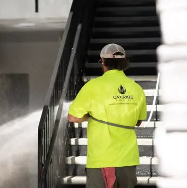 OakRise technician pressure washing multi-family apartment building siding with controlled equipment