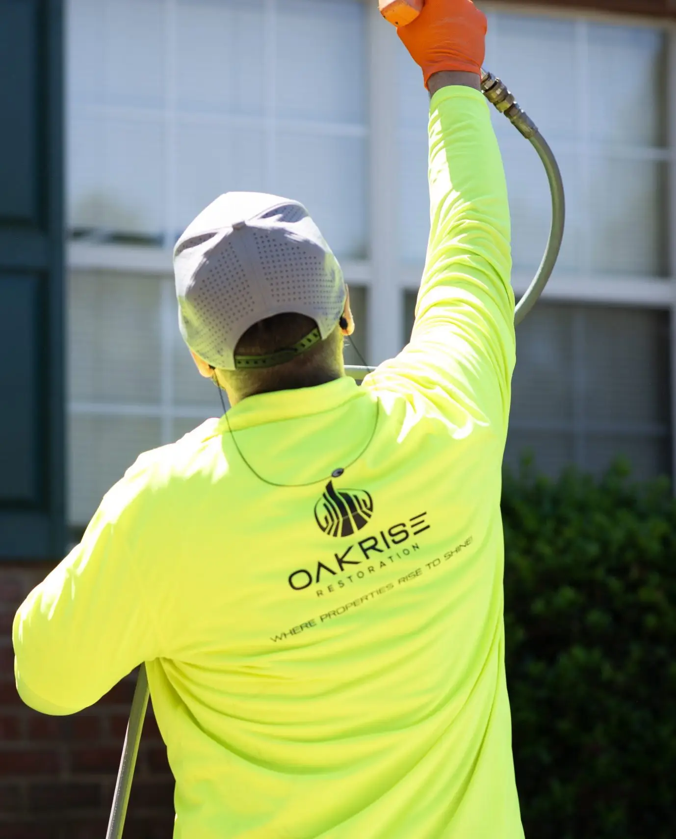 Commercial technician pressure washing multi-story building façade in safety gear