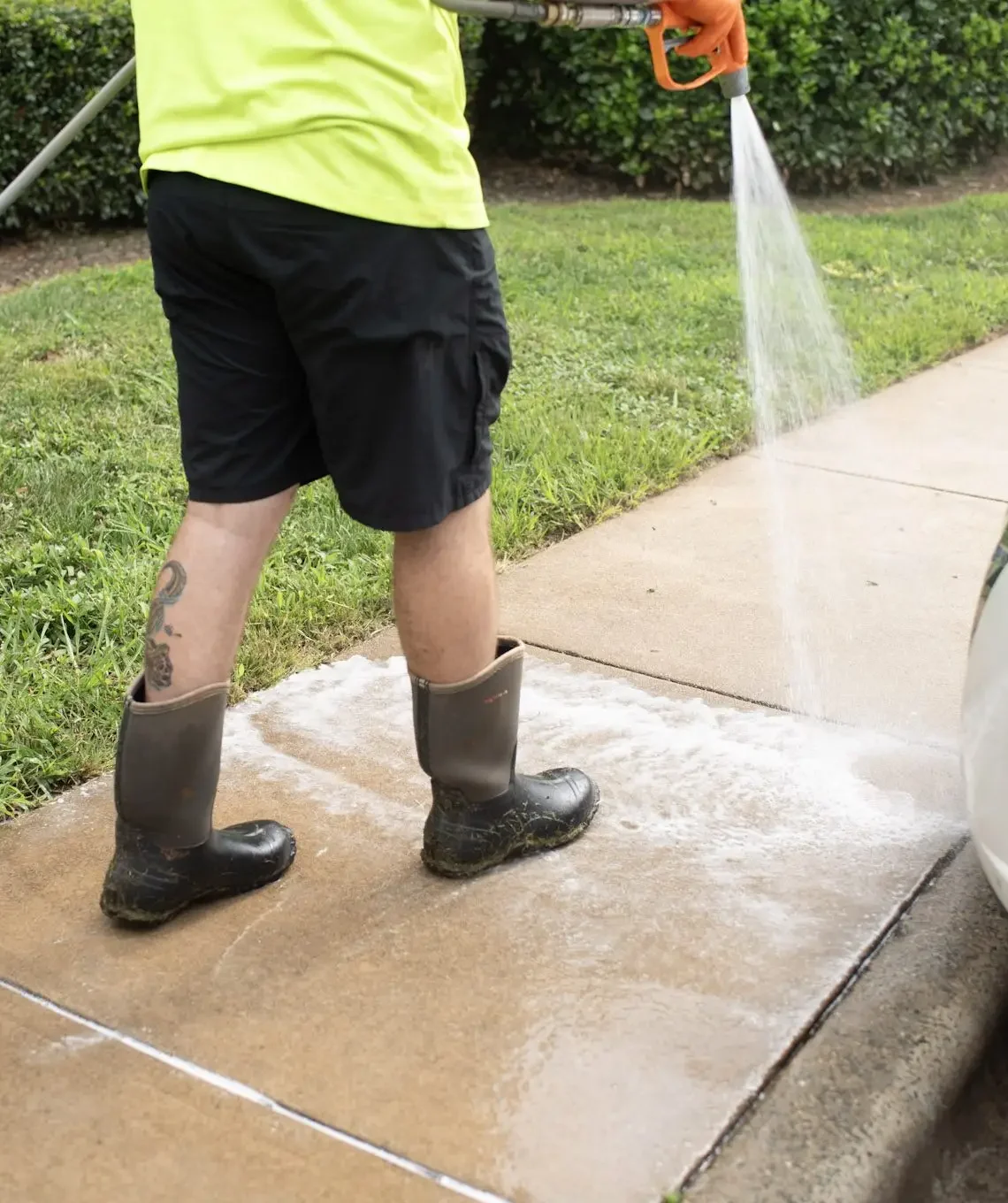 Worker cleaning concrete sidewalk with professional surface washer and detergent