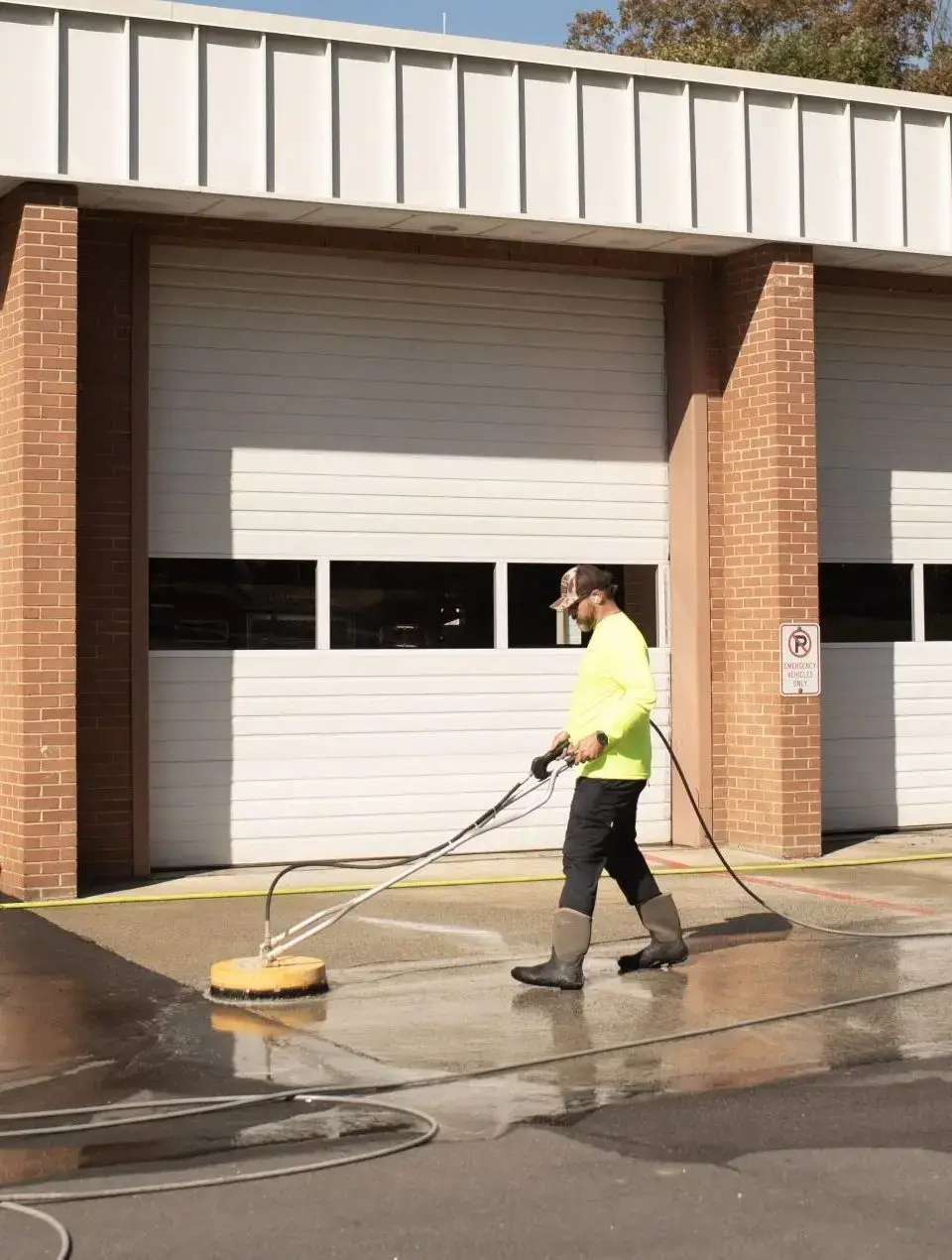 Technician surface cleaning commercial dumpster pad with rotary pressure washer